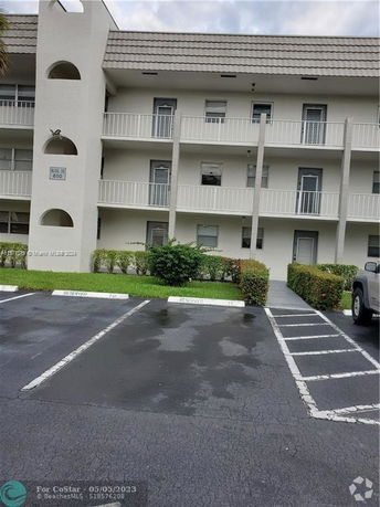 Front view of a multi-story apartment building with balconies and parking spaces.