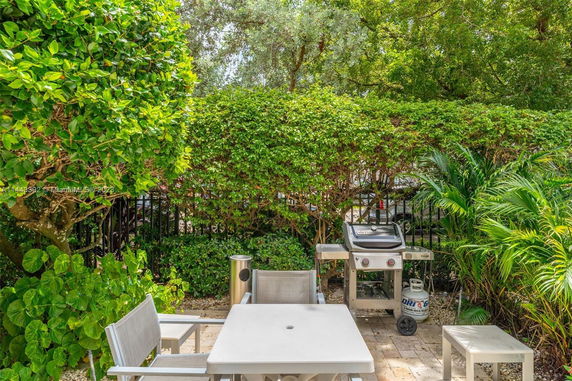 Outdoor patio area with a table, chairs, and a barbecue grill surrounded by greenery.
