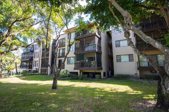 View of a multi-story residential building with balconies surrounded by trees and grassy areas.