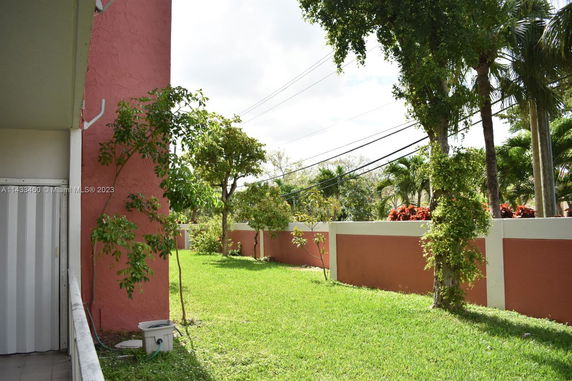 View of green lawn with trees and a pink wall surrounding the area.