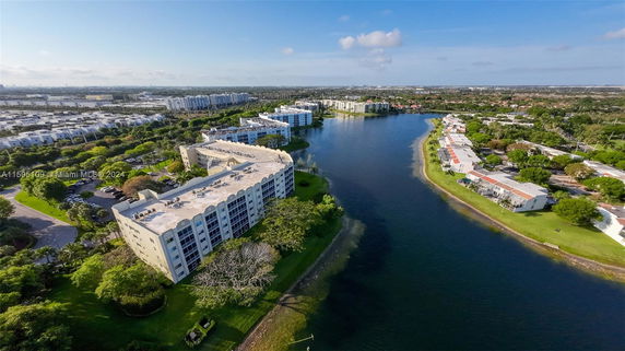 Aerial view of a residential complex by a lake with surrounding greenery and houses.