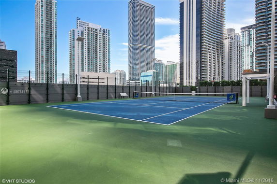 Rooftop tennis court surrounded by high-rise buildings.