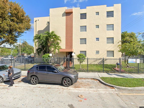 Front view of a three-story building with a fence and parking area in front.
