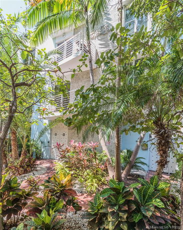 Front view of a multi-story building with balconies and lush green landscaping.