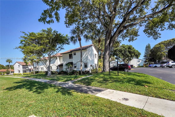 View of a multi-story house with white exterior and red-tiled roof, surrounded by trees and grass.