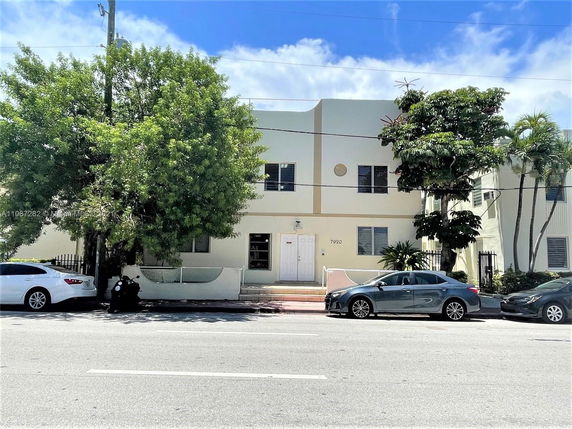 Front view of a two-story building with trees and cars parked in front.