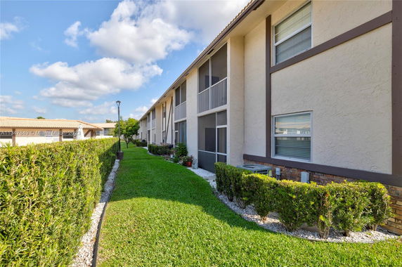 Side view of a two-story building with screened balconies and a landscaped yard.