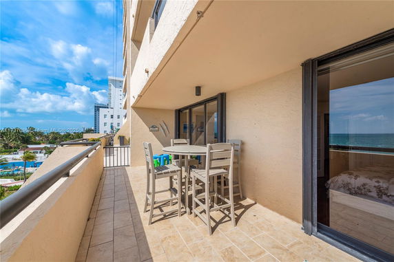 Outdoor patio with table and chairs overlooking ocean view from building.