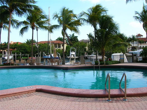 View of a swimming pool area with palm trees and nearby waterfront properties.