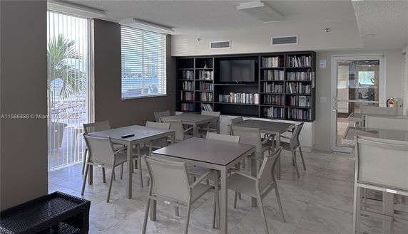Indoor common area with tables, chairs, and a bookshelf with a TV.