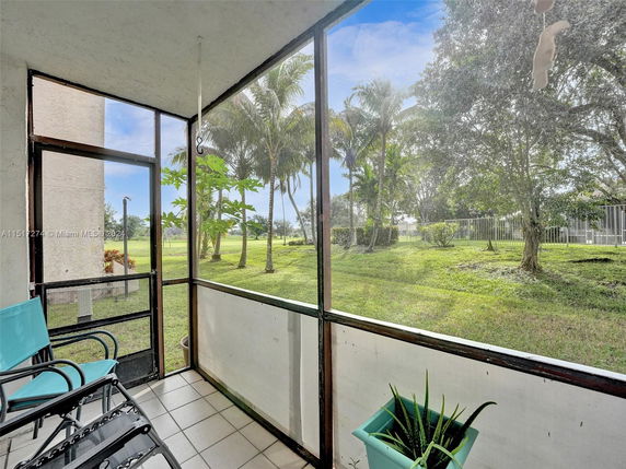 View from a screened porch overlooking a grassy area with trees and a fence.