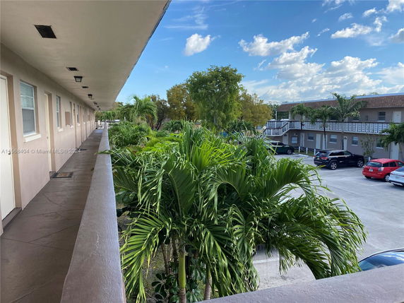 View of a residential complex with surrounding greenery and parked cars in the lot.
