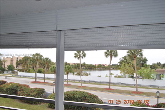 View from a building showing a road, palm trees, and a body of water in the distance.
