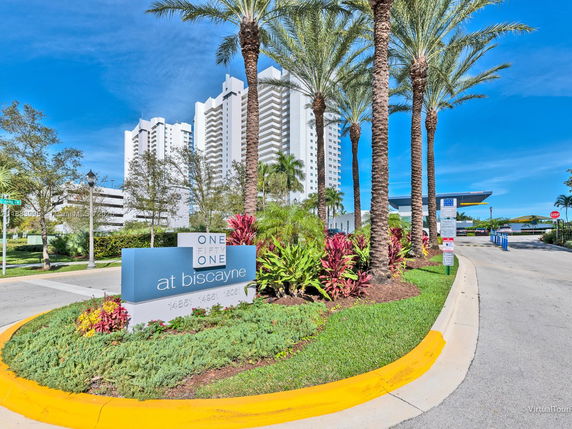 Front view of a tall apartment building with palm trees and signage.