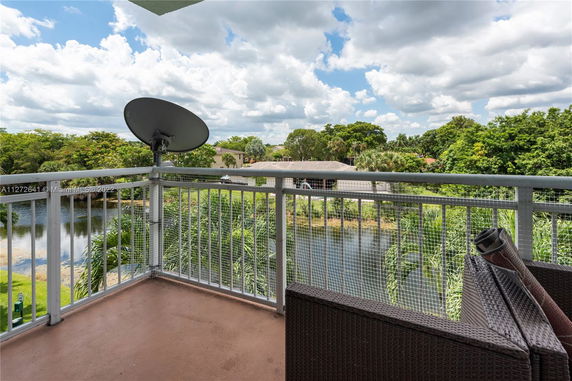 View from a balcony showing a landscape with trees, a pond, and residential buildings in the background.