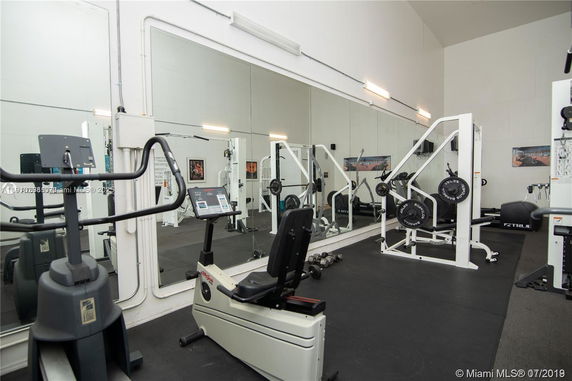 Indoor gym area with various exercise equipment and mirrors on the wall.