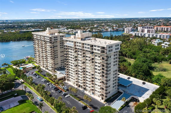 Aerial view of high-rise residential buildings near a waterway, with surrounding greenery and a parking lot.