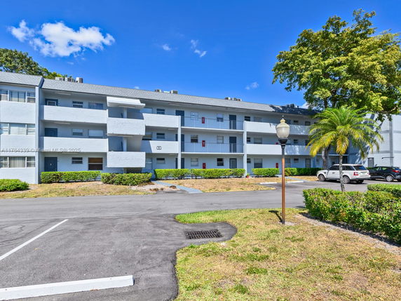 Front view of a multi-story apartment building with balconies and a parking area.