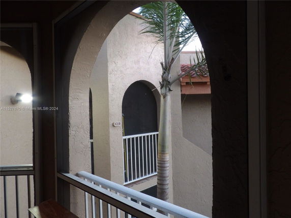 View from a building showing arches and a palm tree in an outdoor hallway.