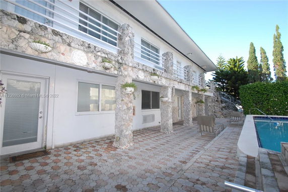 Outdoor view of a two-story building with stone columns and a swimming pool on the right.