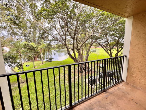 Balcony view overlooking trees and a pond with grassy areas.