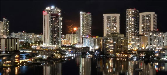 Nighttime view of high-rise buildings with lights and reflections on a body of water.