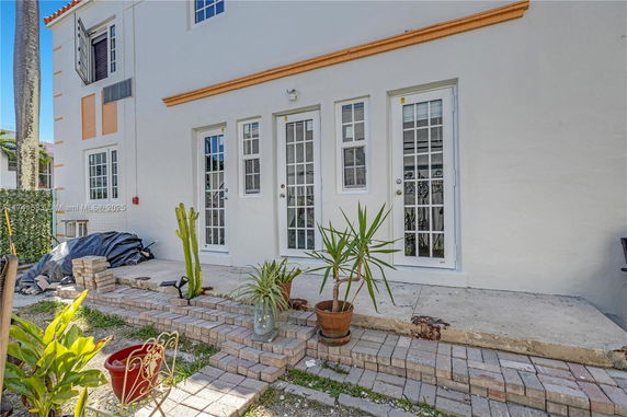 Front view of a multi-story house with multiple French doors and potted plants on a paved area.