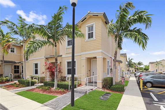 Front view of a two-story house with light-colored exterior and decorative plants.