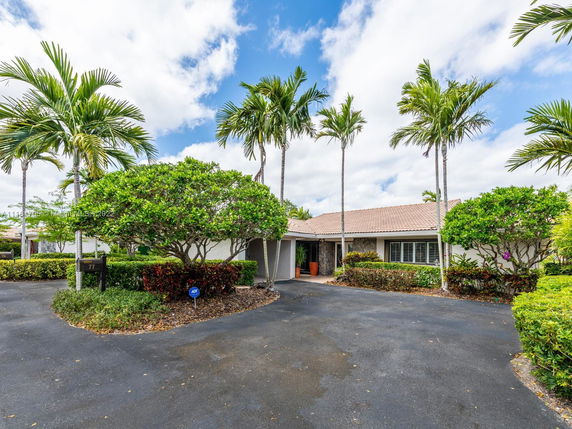 Front view of a single-story house with a tiled roof and surrounding palm trees.
