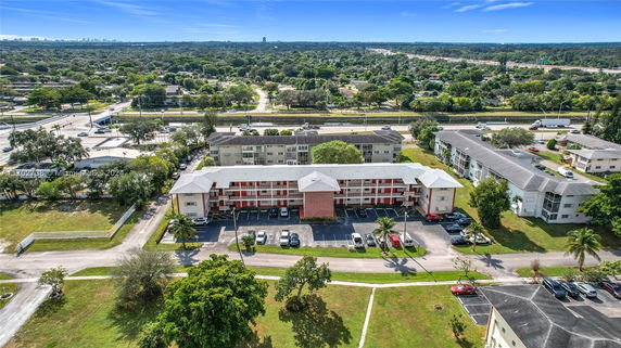 Aerial view of a residential building with a parking area in front, surrounded by roads and greenery.