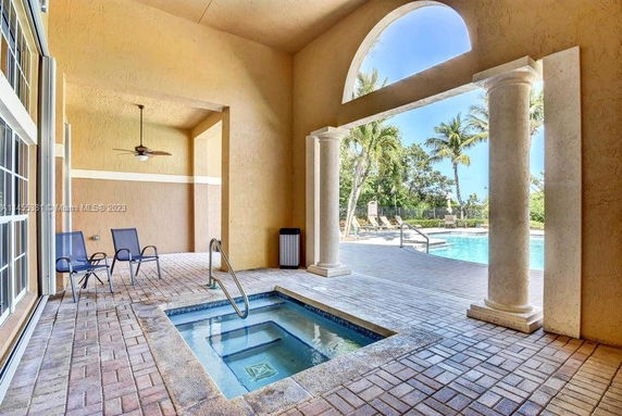 Covered patio area with a small pool and view of an outdoor swimming pool surrounded by palm trees.