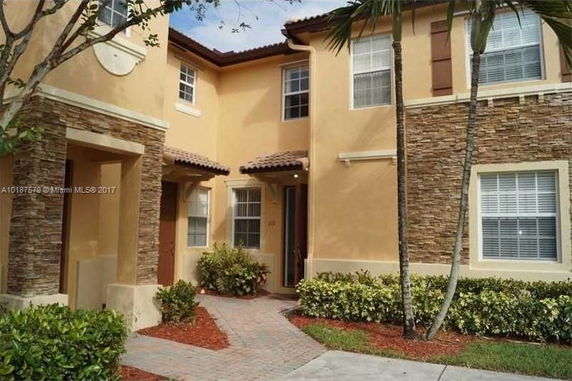 Front view of a two-story townhouse with tan stucco exterior and stone accents.