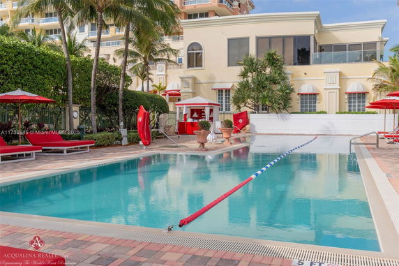 Outdoor swimming pool area with lounge chairs and umbrellas near a building.