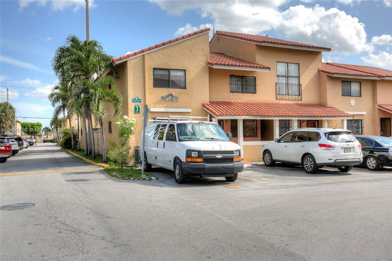 Front view of a two-story townhouse with a sloped roof and multiple parked vehicles.