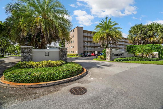 Front view of a multi-story residential building with palm trees and gated entrance.