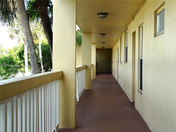 Exterior corridor of a building with railing and palm trees visible.