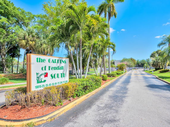 Entrance view of The Gardens of Kendall South with palm trees and a driveway.