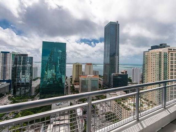Panoramic view of a cityscape from a balcony, featuring tall skyscrapers and a distant view of the water.