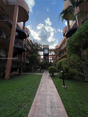 View of a multi-story building with balconies and a garden pathway leading to the entrance.