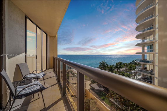 Balcony with chairs overlooking the ocean and nearby buildings.