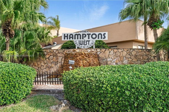 Front view of a condominium building with a stone wall and sign.