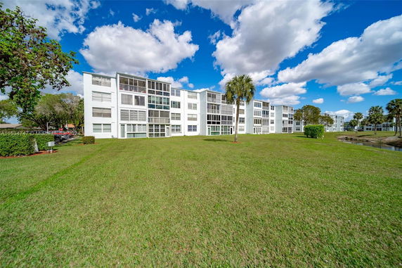 View of multiple apartment buildings with large windows and open grassy area in front.