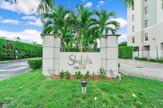 Entrance sign of Sky Lofts building with greenery and palm trees.