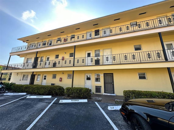 Front view of a three-story building with balconies and a parking area in front.