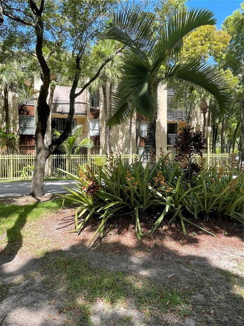 View of a multi-story building with balconies surrounded by trees and plants.