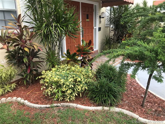 Front view of a house entrance with a brown door and surrounding greenery.