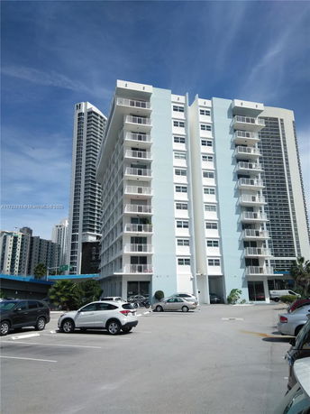 Front view of a multi-story building with balconies and parking area.