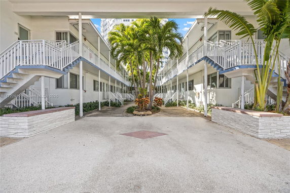Front view of a two-story building with exterior staircases and central palm trees.