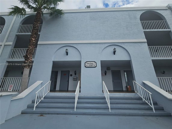 Front view of a multi-story building with balconies and an entrance staircase.