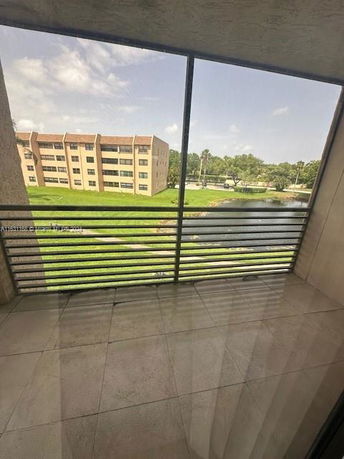 View from a building balcony overlooking grassy area and pond with other buildings in the background.